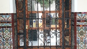 A large wooden door with intricate ironwork, set in a stone-tiled entrance area with decorative tile panels on either side. - Pensión Catedral (Seville)