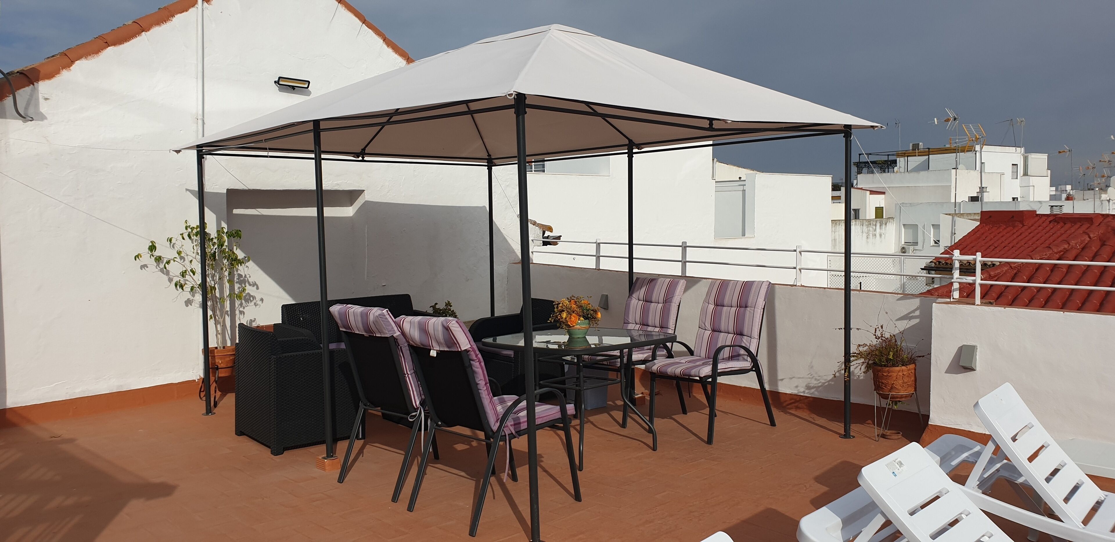 Una terraza en la azotea con una zona de estar techada, una mesa y sillas.