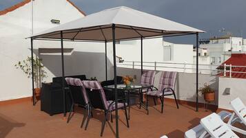 Una terraza en la azotea con una zona de estar techada, una mesa y sillas.