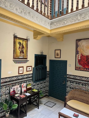 A room with a blue door, a framed picture, a table with books, and a wicker sofa. - Pensión Catedral (Seville)