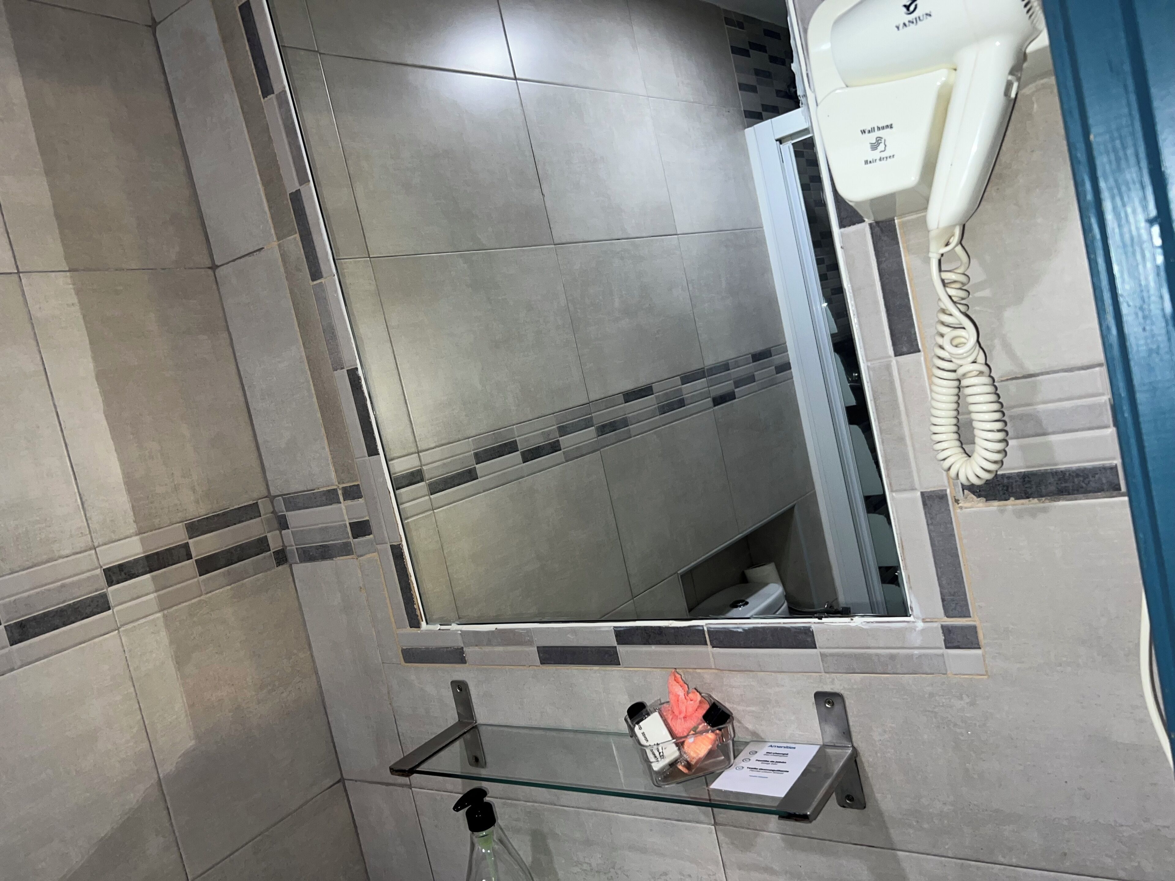 Een badkamer met een spiegel, een haardroger en een glazen plankje met toiletartikelen.