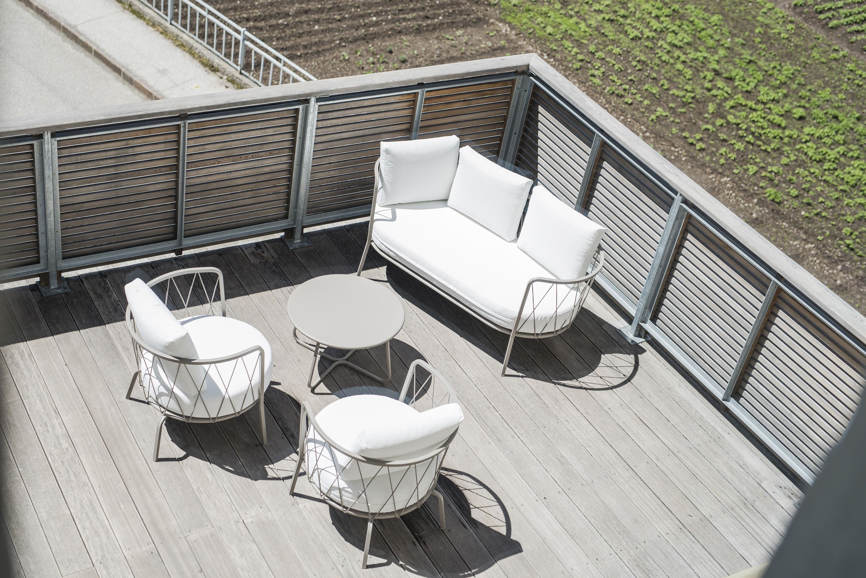 A deck with a white sofa, two white chairs, and a small round table.