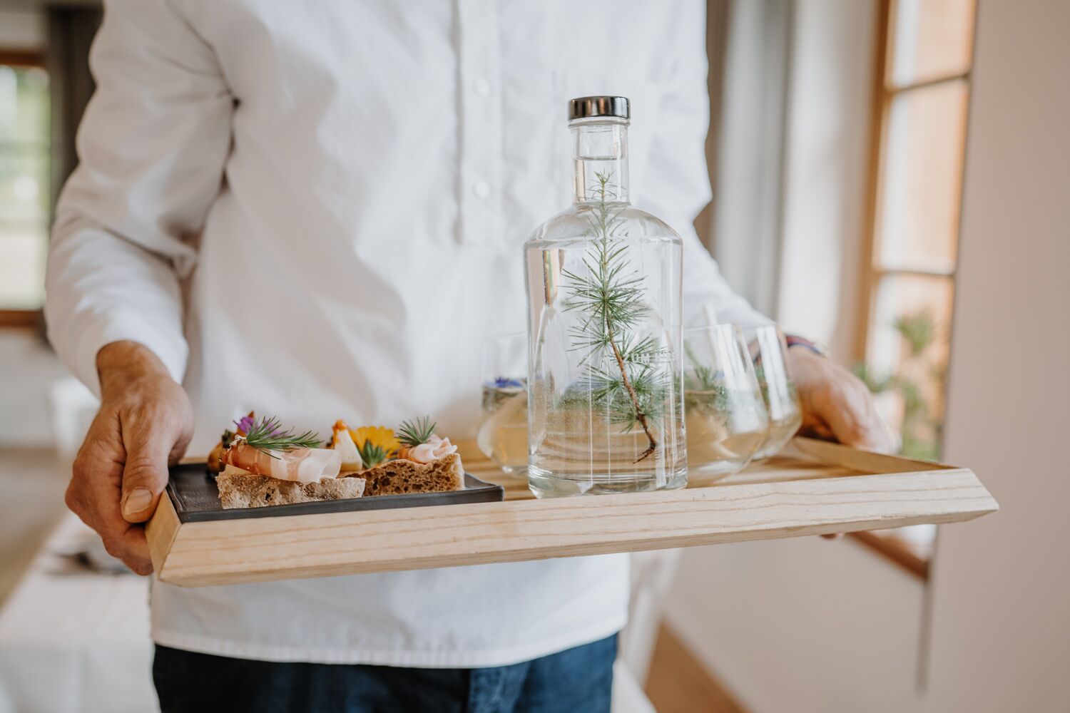 A person holding a tray with food and a glass bottle with a plant.