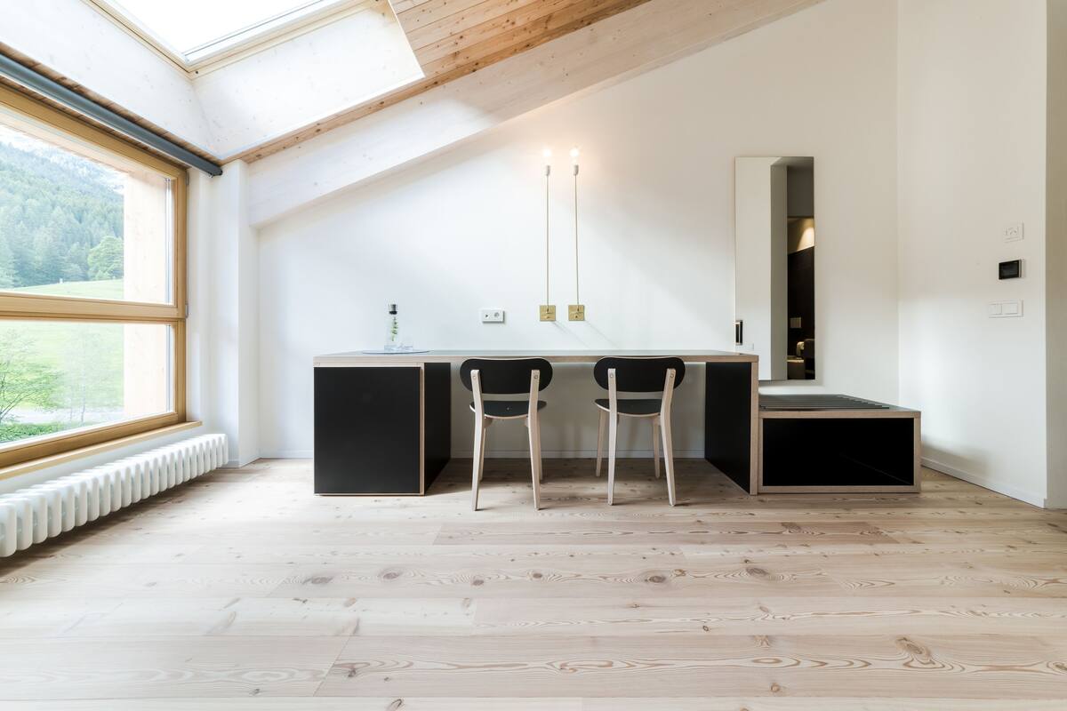 Una habitación moderna con tragaluz, un escritorio negro con dos sillas y un espejo grande.