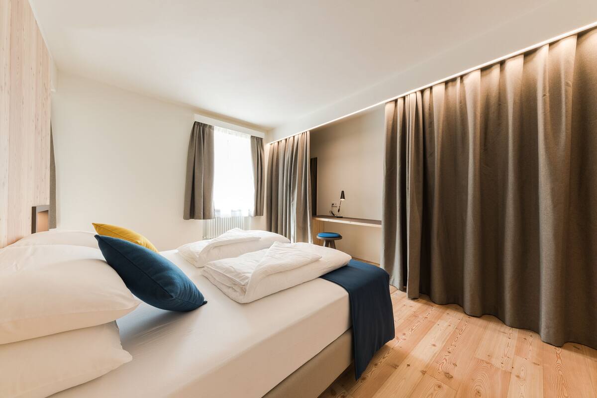 Una cama bien hecha con almohadas, una mesita de noche y una ventana con cortinas.