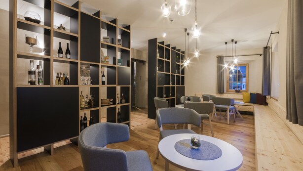 Un intérieur moderne avec un plancher en bois, une table ronde centrale entourée de chaises, et des étagères intégrées où sont exposées des bouteilles de vin et des verres.