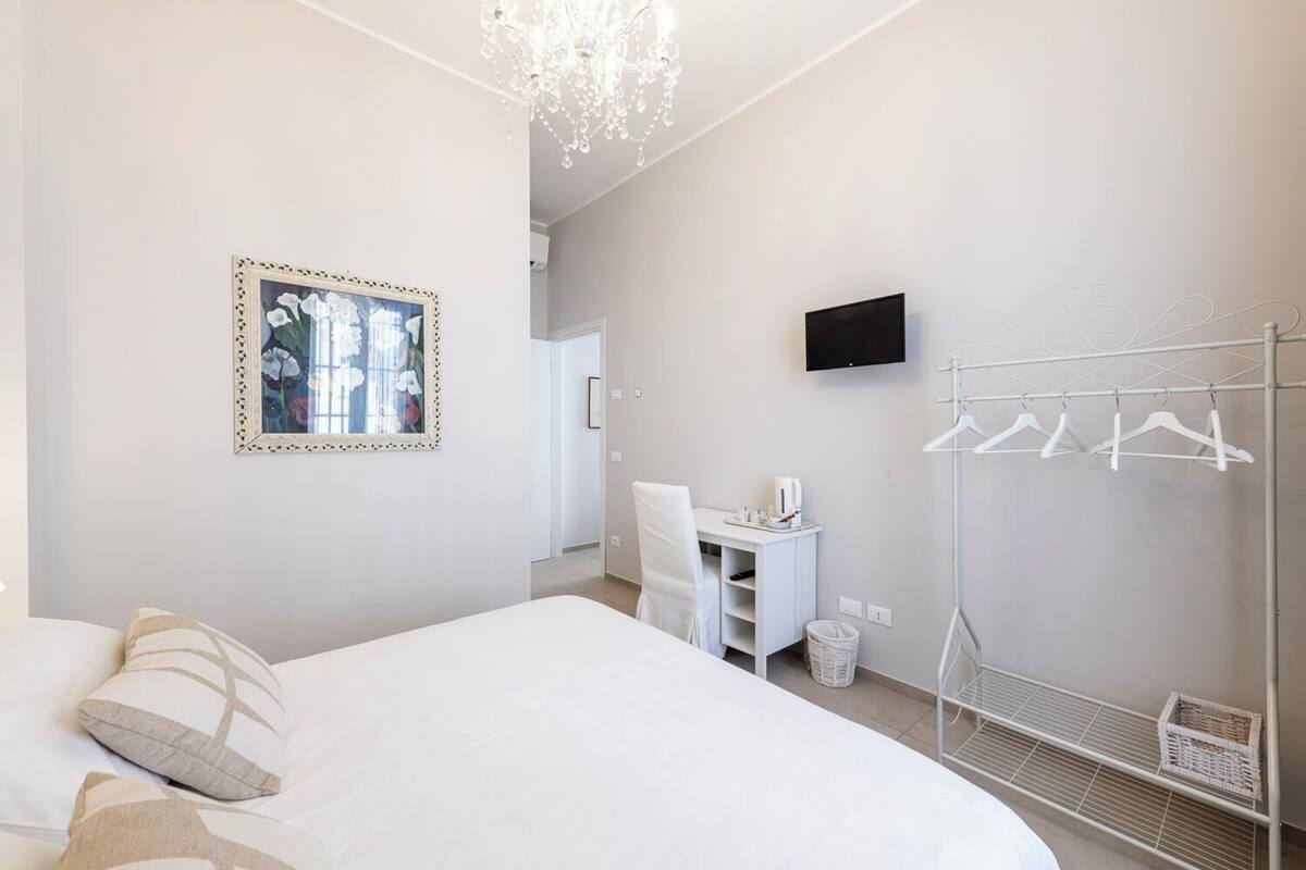A hotel room with a bed, a desk, a chair, a TV, and a clothing rack.