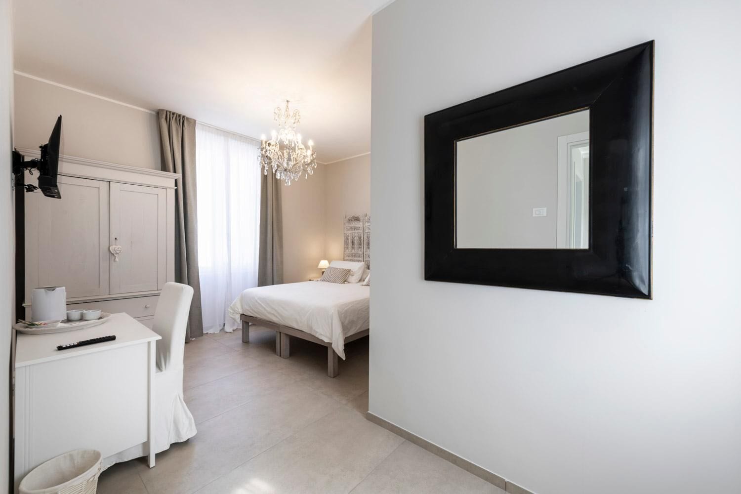 Un dormitorio con cama, mesita de noche, silla y un espejo grande en la pared.