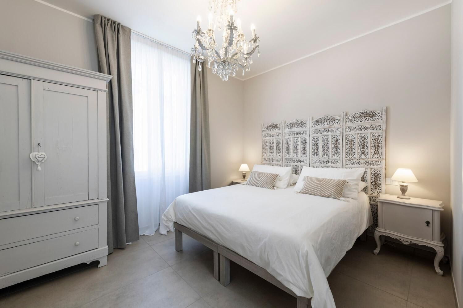 Un dormitorio con una cama grande, un armario, una araña y un cabecero decorativo.