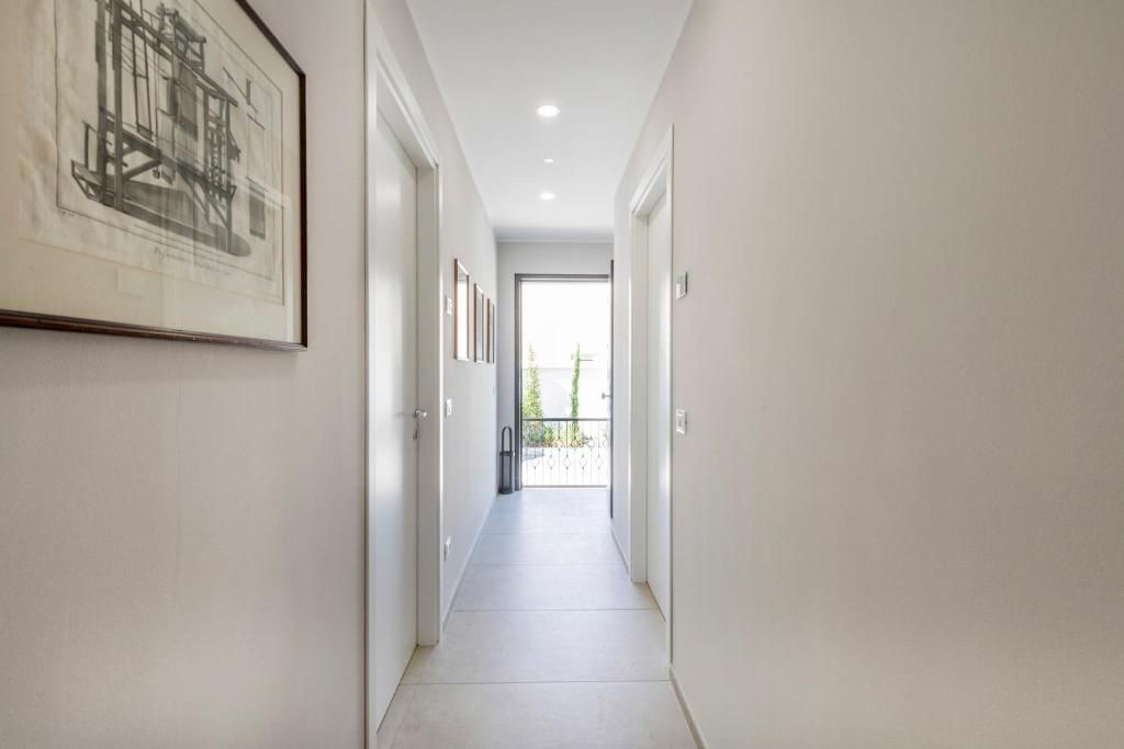 A narrow hallway with white walls, a tiled floor, and a framed architectural drawing on the left.