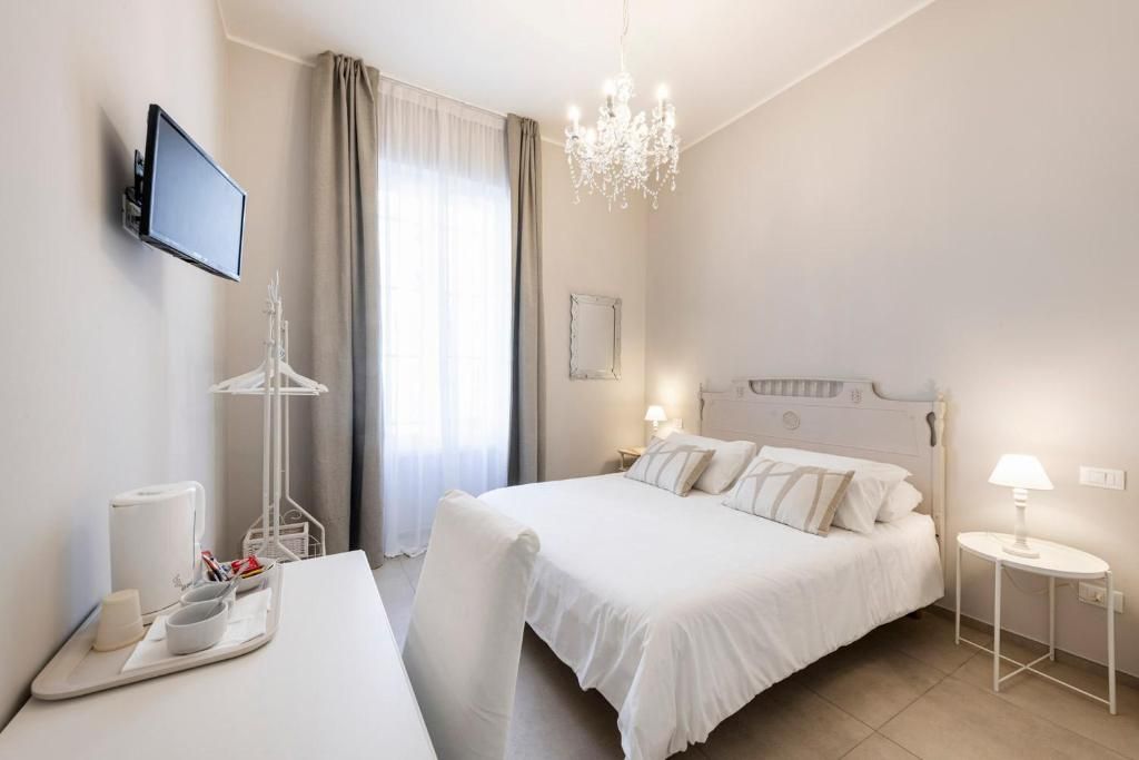 Quarto de hotel com cama, mesas de cabeceira, televisão, lustre e janela com cortinas.