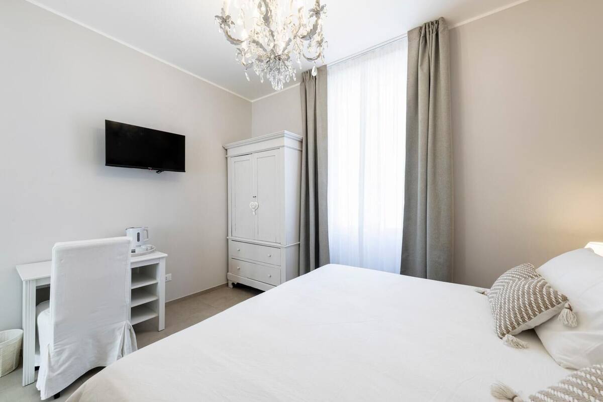 A hotel room with a bed, a TV mounted on the wall, a desk with a chair, and a wardrobe.