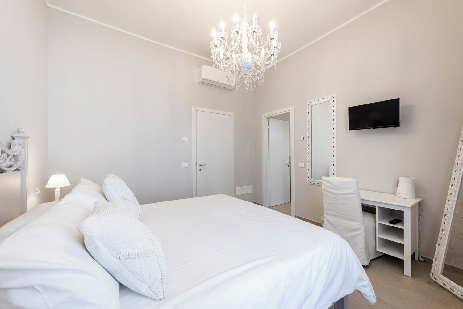 A bedroom with a large bed, a desk, a chair, a TV, and a mirror.