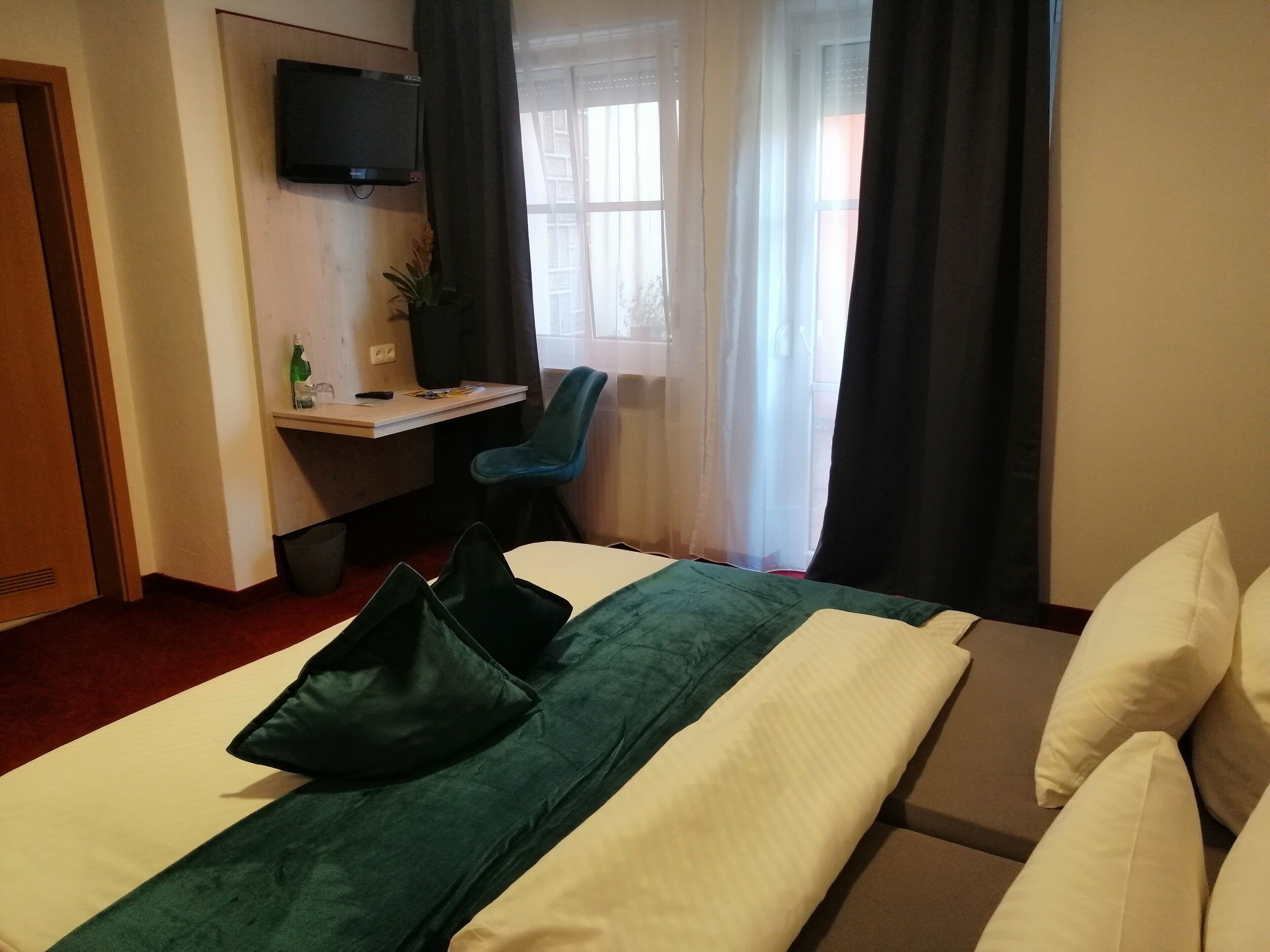 Ein Hotelzimmer mit einem Bett, einem Schreibtisch, einem Stuhl und einem an der Wand montierten Fernseher.