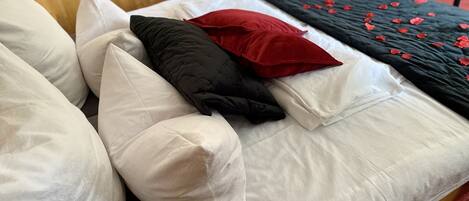 A neatly made bed with white and black pillows, a red accent pillow, and a black bedspread with red floral patterns.