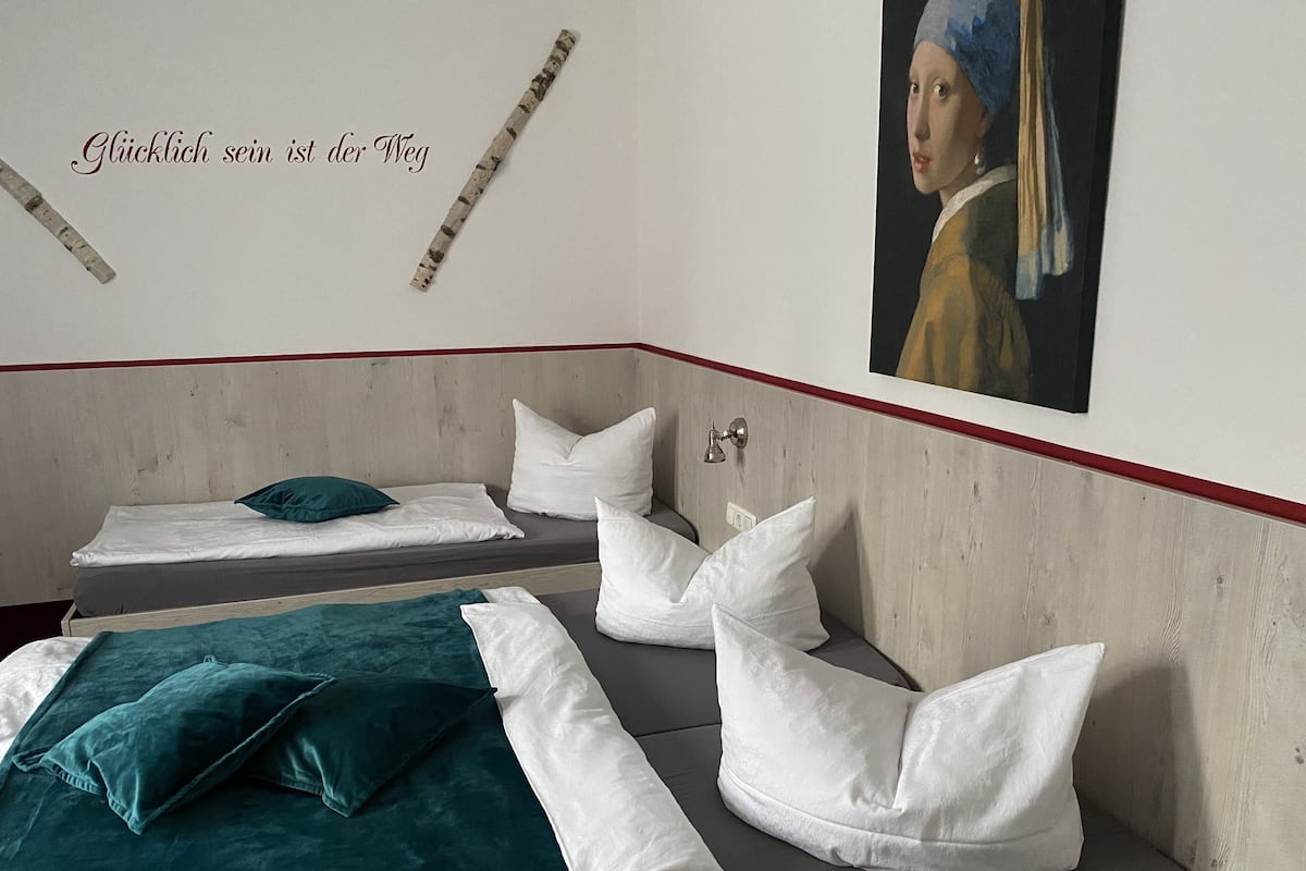 A hotel room with two beds, one with teal bedding and the other with white bedding. There is a painting on the wall and a wooden headboard.