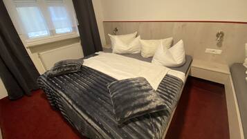 Una habitación de hotel con cama, mesita de noche, ventana con cortinas y un radiador.