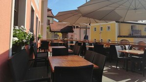 Un café en plein air avec des tables et des chaises, des parasols et un bâtiment à la façade jaune.