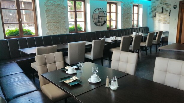 Un restaurant avec des tables et des banquettes en bois foncé, des murs en pierre et de grandes fenêtres.
