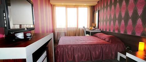 Una habitación de hotel con una cama, un escritorio con computadora, televisión y ventana con cortinas.