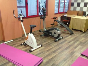 Un gimnasio con equipo de ejercicio, incluyendo una elíptica y una bicicleta estática, una mesa con sillas y colchonetas rosas en el suelo.