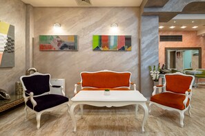 Un área de recepción con pared de mármol, dos sofás de tapicería contrastante y dos lámparas fijadas a la pared.