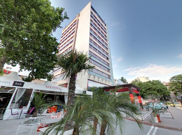 Un edificio moderno con un letrero llamativo, rodeado de palmeras y zonas de estar al aire libre.