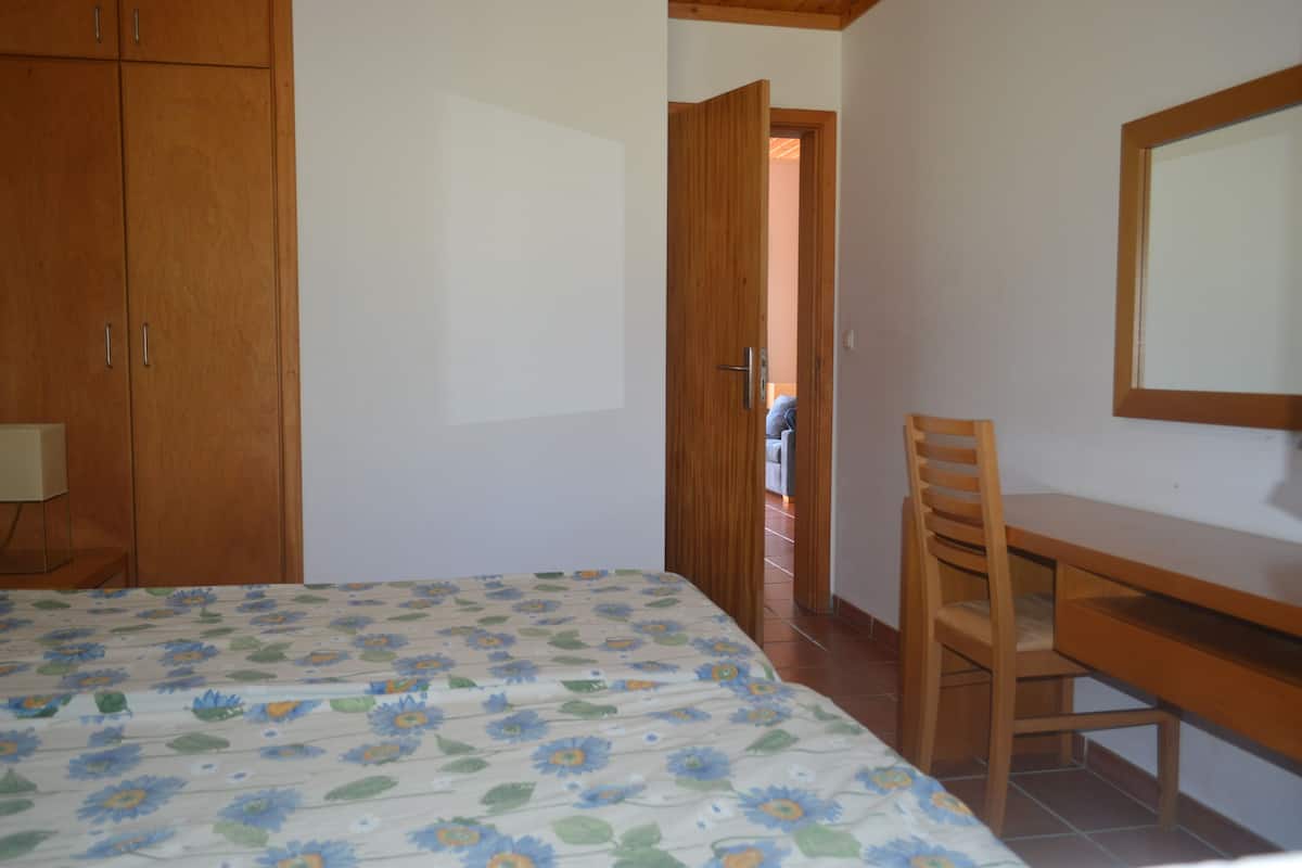 A bedroom with a bed, wooden wardrobe, and a desk with a chair.