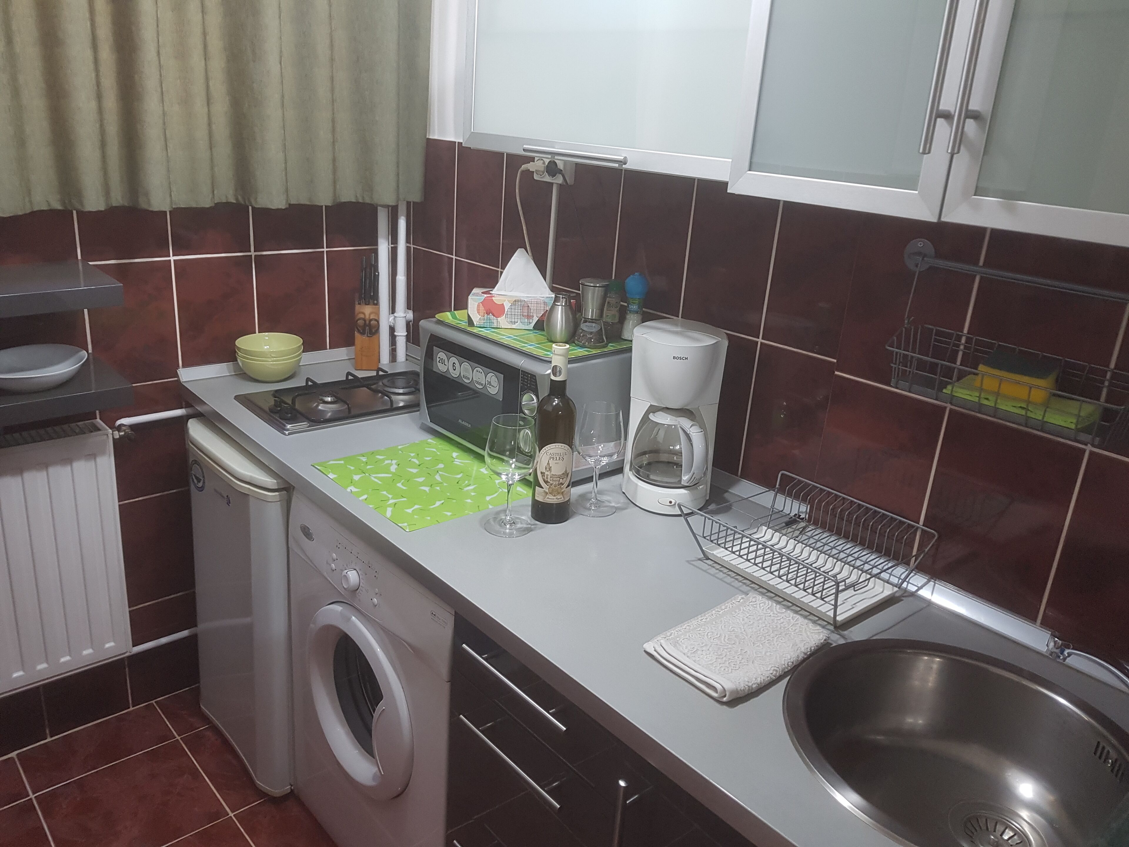 A compact kitchen with a washing machine, a microwave, a coffee maker, and a sink.