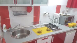 Een keuken met een spoelbak, fornuis, magnetron en keukenkastjes.
