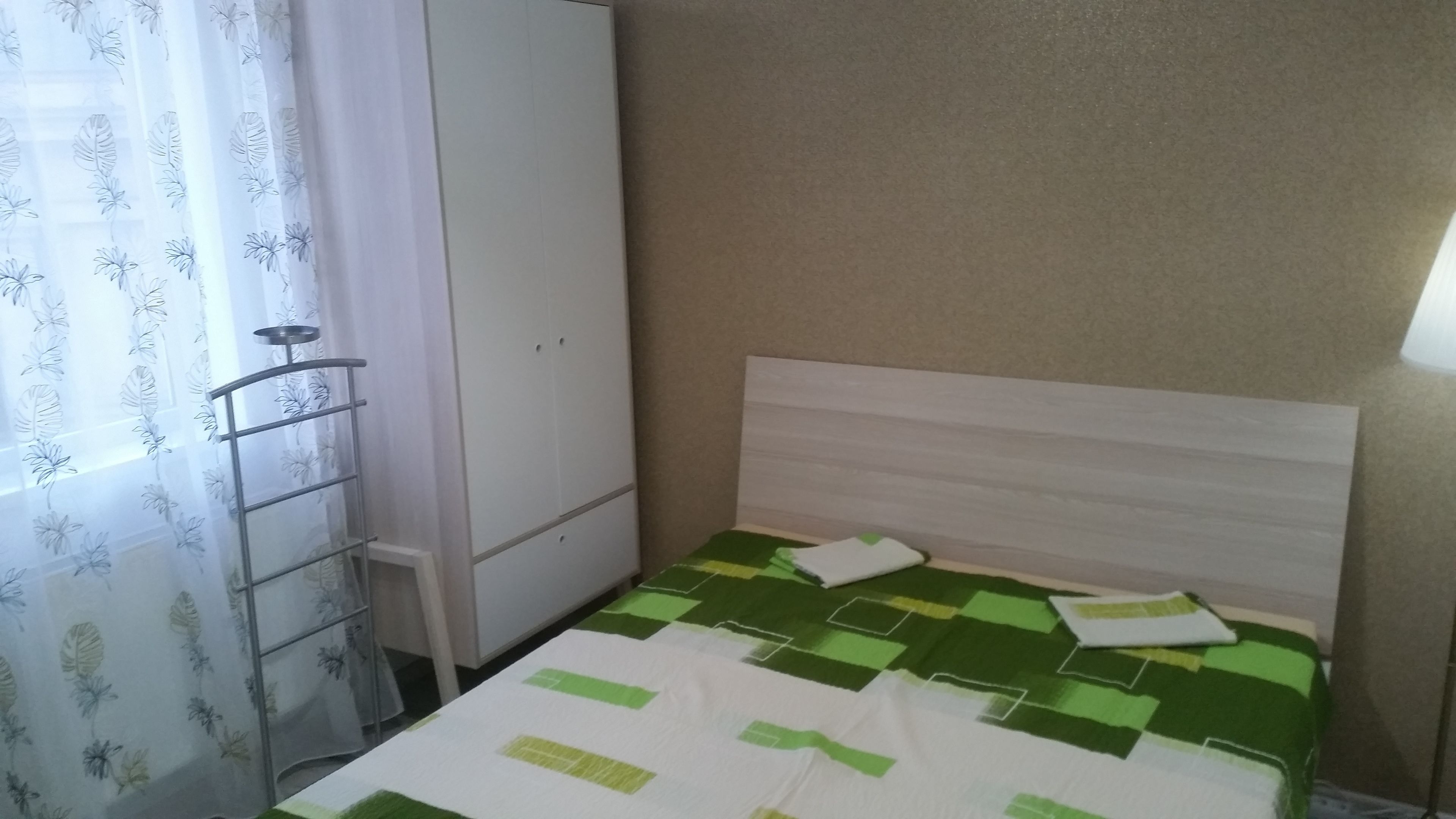 Ein Zimmer mit einem Bett, einem Kleiderschrank, einer Heizung und einem Fenster mit Vorhängen.
