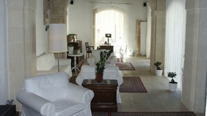 A spacious room with a white sofa, a wooden table, and a dining area with a chandelier. - B&B La Via della Giudecca (Syracuse)