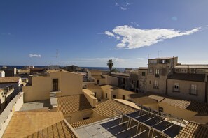 A rooftop terrace with multiple levels of seating, a palm tree, and a view of the sea.
