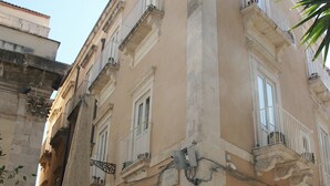 A historic building with classical architecture, featuring ornate balconies and a large central column. - B&B La Via della Giudecca (Syracuse)