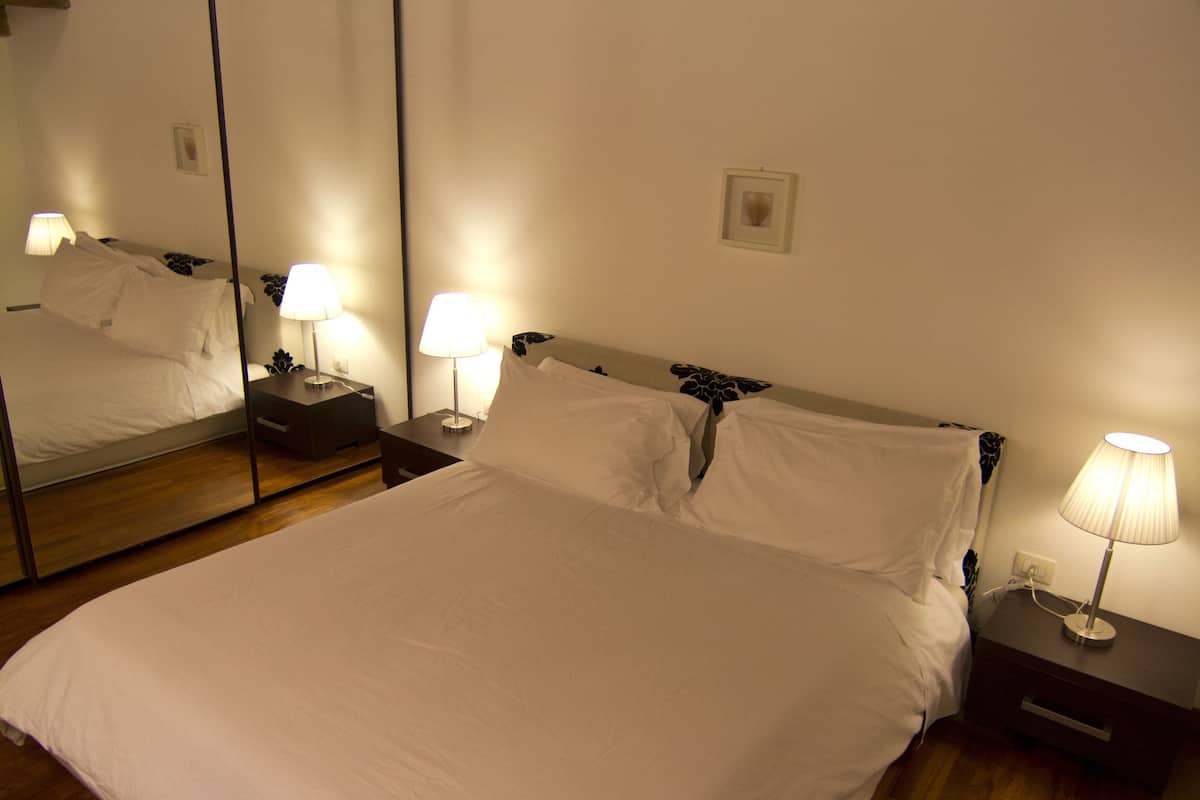 Un lit bien fait, avec du linge de lit blanc, une tête de lit en bois et des lampes de chevet.