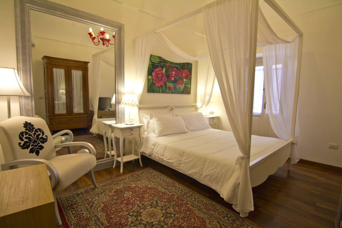 Une chambre à coucher avec un lit à baldaquin, une table de chevet, une chaise, un bureau et un grand miroir.