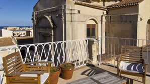 A rooftop terrace with wooden furniture, potted plants, and a view of the sea. - B&B La Via della Giudecca (Syracuse)