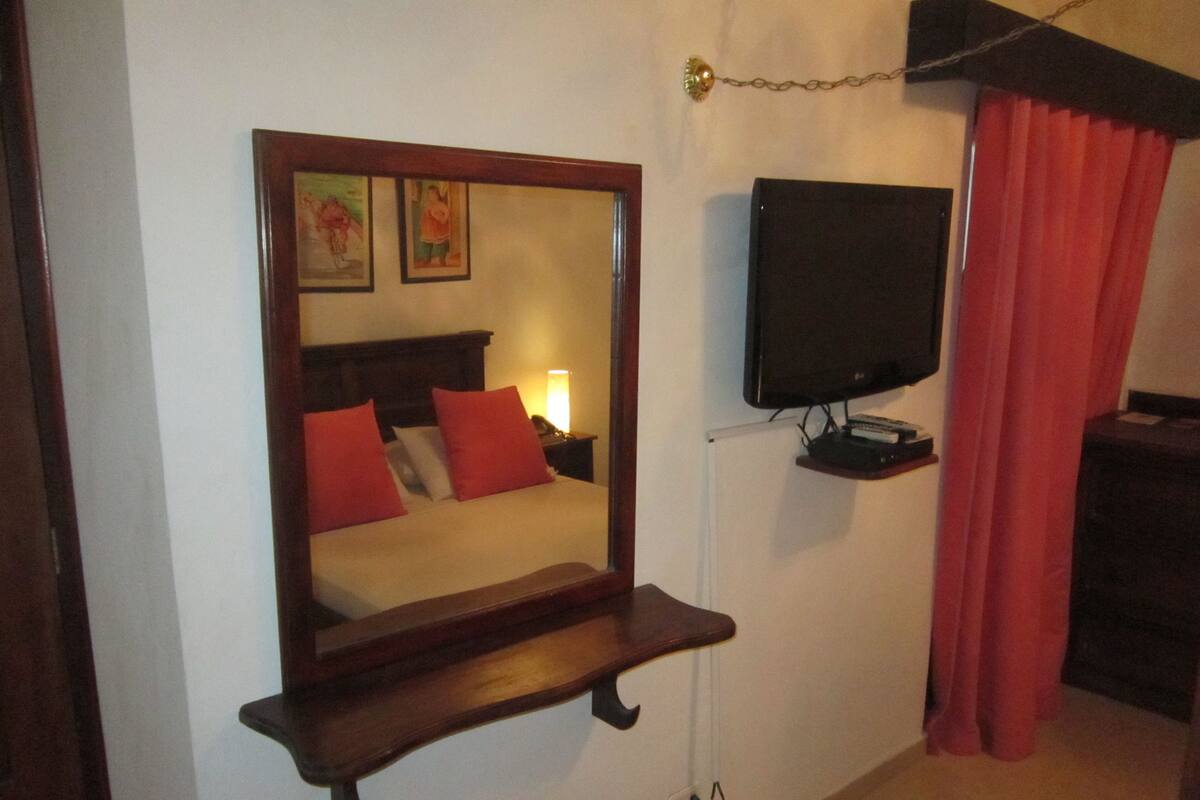 A bedroom with a bed, a TV mounted on the wall, and a mirror with a wooden frame.