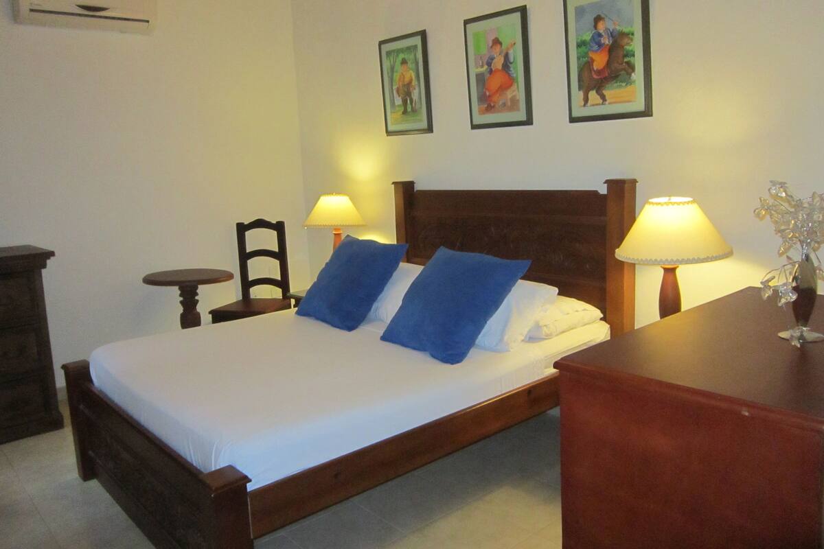 A neatly made bed with blue pillows, a wooden headboard, and two bedside lamps. There are three framed pictures on the wall above the bed.