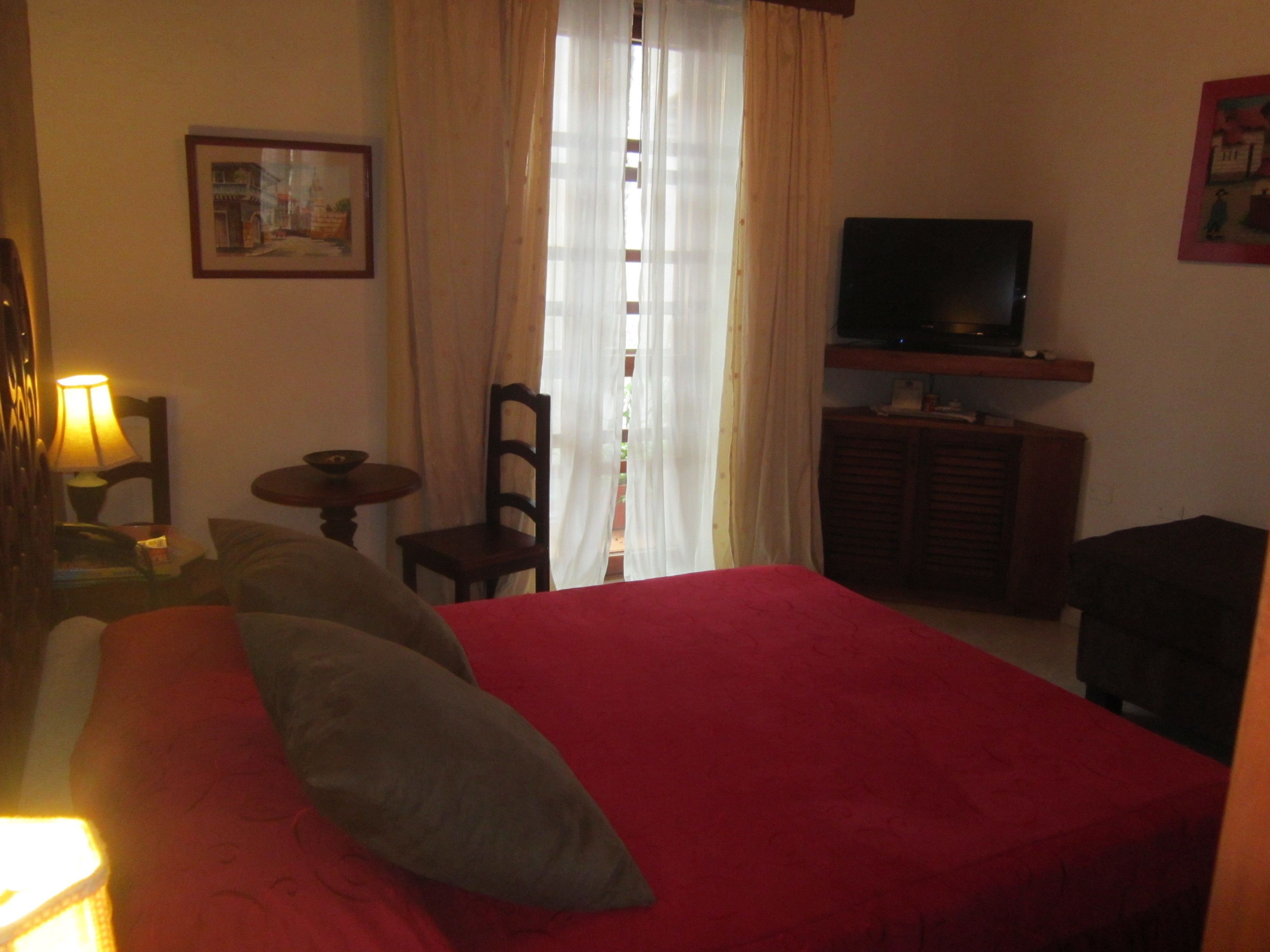 A hotel room with a large bed, a television on a wooden cabinet, a small table with a lamp, and a chair.