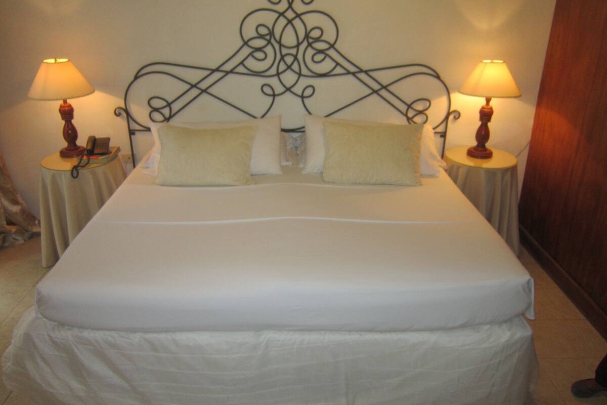 A neatly made bed with two pillows, a decorative metal headboard, and two bedside lamps on matching tables.