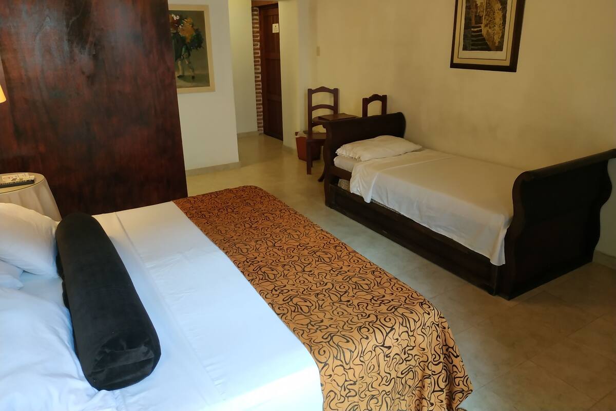 A hotel room with two beds, a wooden wardrobe, a chair, and a painting on the wall.