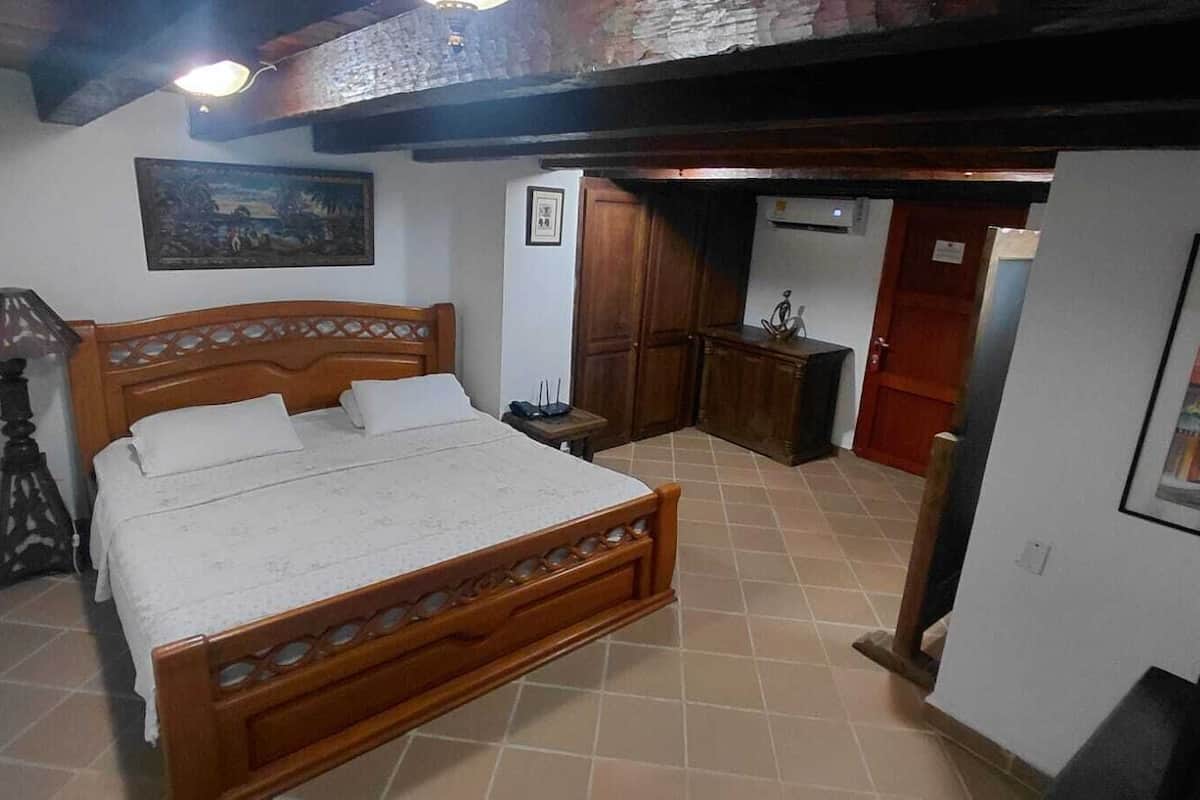 A bedroom with a wooden bed, a nightstand, a lamp, and a painting on the wall.