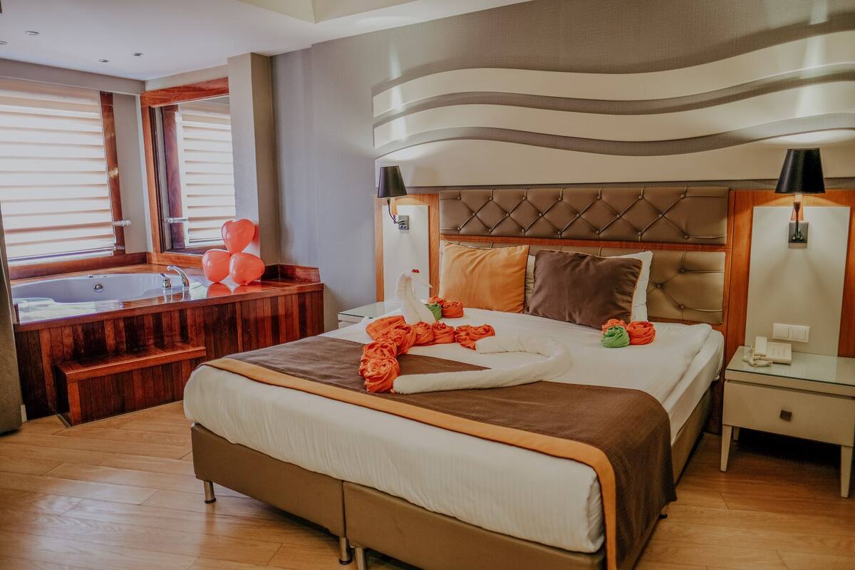 Een hotelkamer met een groot bed, een houten bank, een badkuip en uitzicht op het groen.
