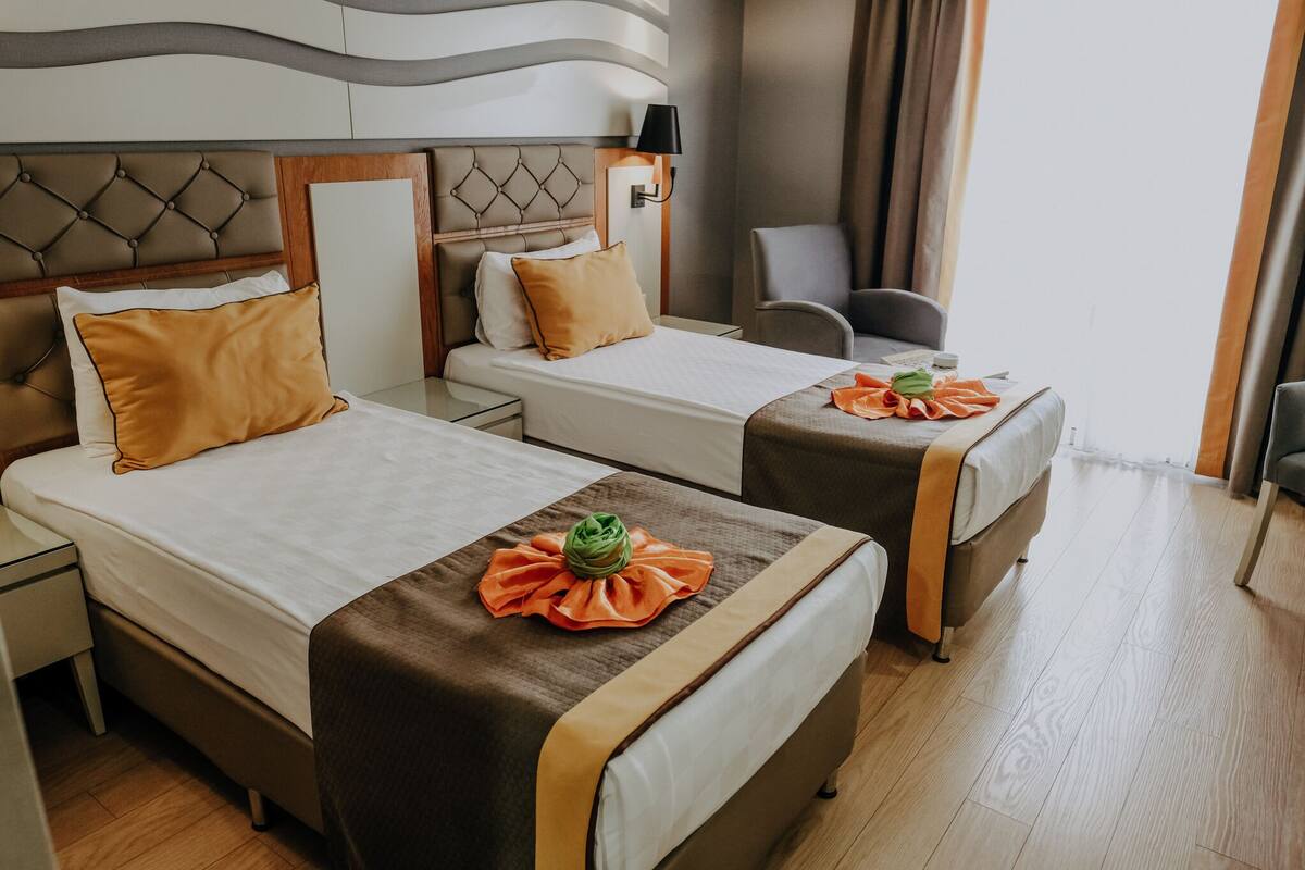 Hotelkamer met twee bedden, elk met een bruin hoofdeinde, nachtkastje, lamp en stoel.