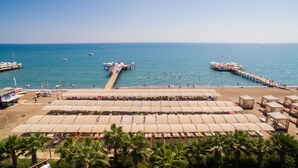 Una spiaggia con file di lettini e ombrelloni, un molo che si protende verso il mare e palme sullo sfondo.