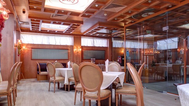 Ein Restaurant mit Holztischen, weißen Tischdecken und einer Glaskabine.