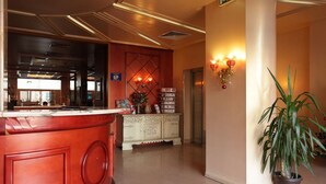 Eine Hotelhalle mit einer Rezeption, einem Dekorationsschrank, einer Topfpflanze und einer Wandleuchte.