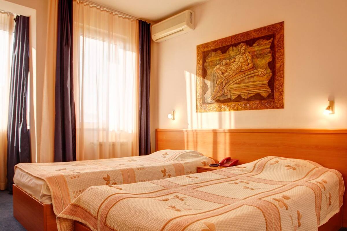 A hotel room with two beds, a painting on the wall, and a window with curtains.