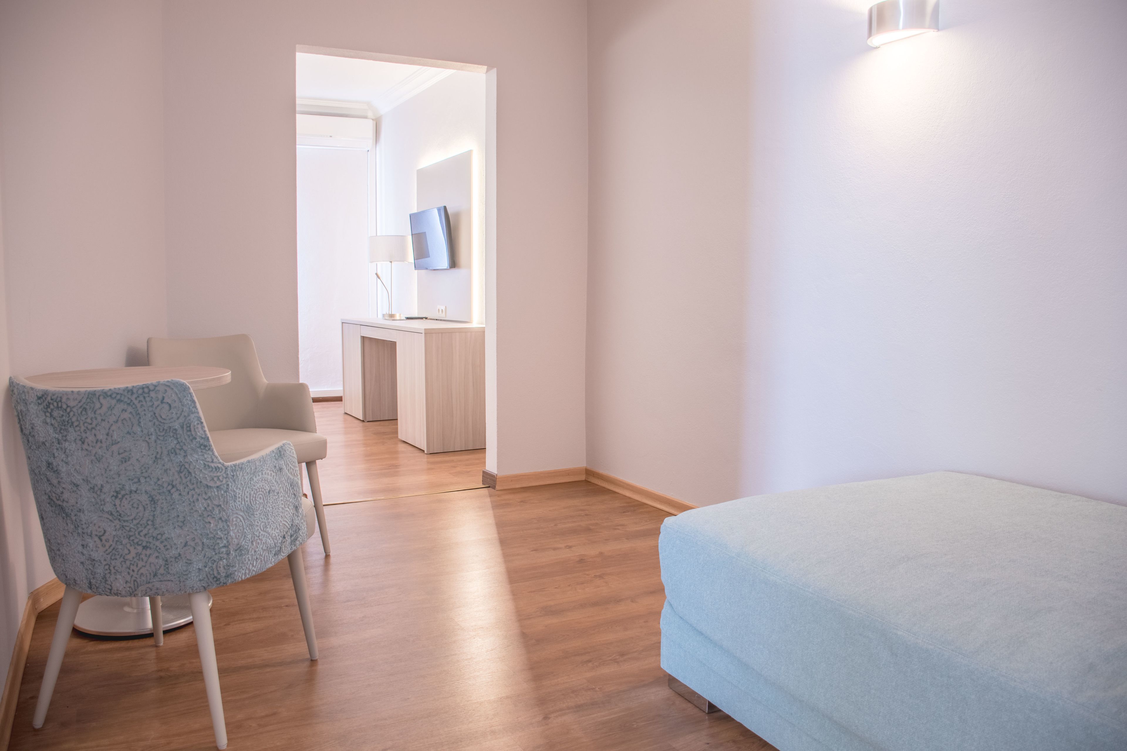 A bedroom with a bed, a chair, and a desk with a lamp.